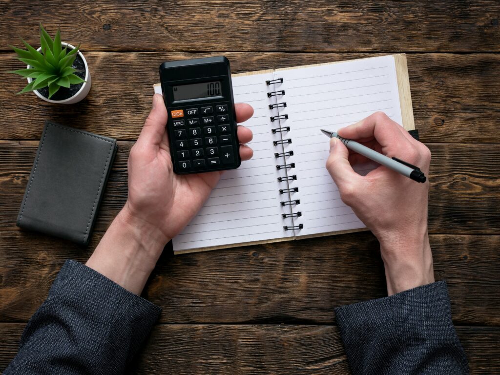 Business man is counting money on a calculator and is writing a sum in a notebook with a blank pages. Accountant.