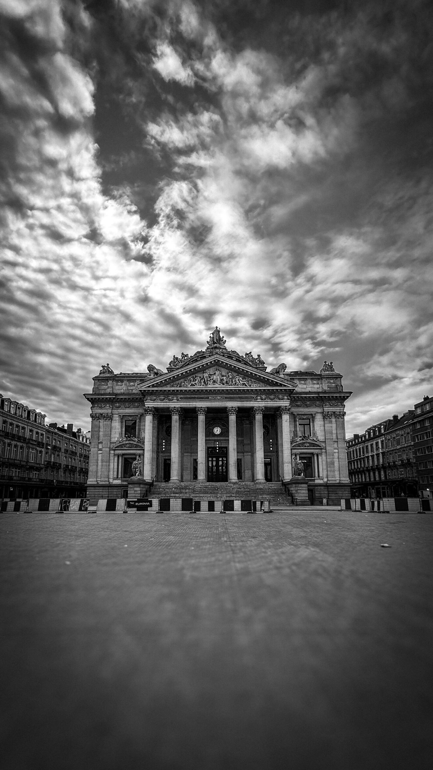A striking black and white image of Brussels Stock Exchange building under dramatic clouds.