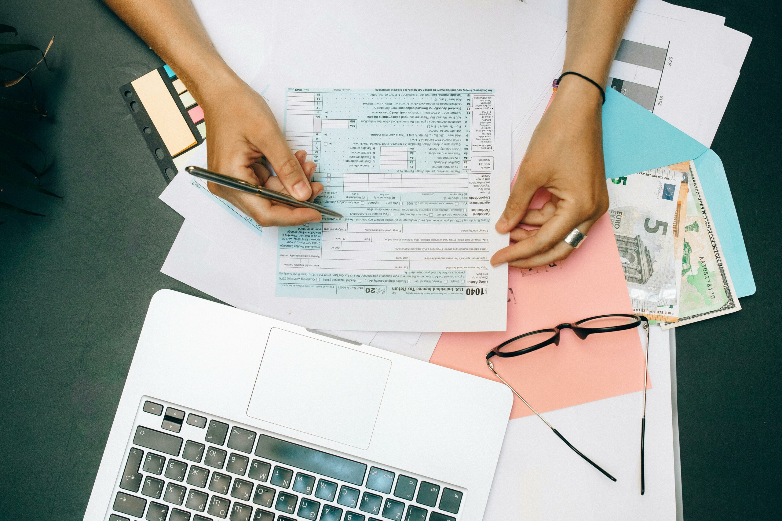Une personne remplit des documents fiscaux sur un bureau avec ordinateur