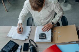 Un homme examine des documents à son bureau avec une calculatrice.